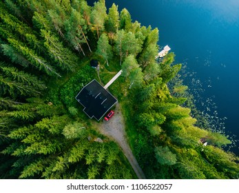 Aerial View Of Wooden Cottage In Green Pine Forest By The Blue Lake In Rural Summer Finland