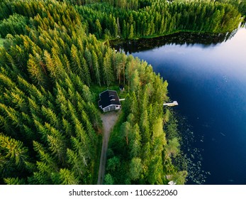 Aerial View Of Wooden Cottage In Green Pine Forest By The Blue Lake In Rural Summer Finland