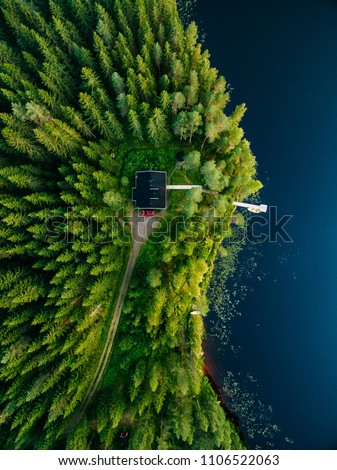 Aerial view of wooden cottage in green pine forest by the blue lake in rural summer Finland