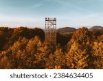 Aerial view of a wooden lookout tower in autumn nature. People stand on the observation tower, enjoying the beautiful, serene view of the surrounding landscape.