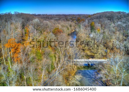 Aerial View of Woods in Fall Colors with a Road, Stream and House
