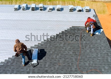 Aerial view in worker hands installing bitumen roof shingles with air hammer and nail