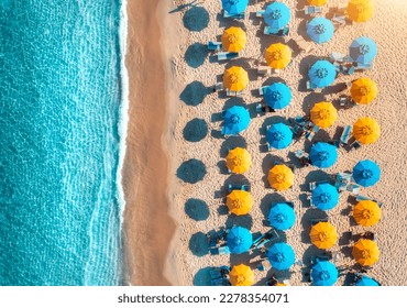 Aerial view of yellow and blue umbrellas on empty sandy beach, blue sea at sunset in summer. Tropical landscape with turquoise water. Travel and vacation in Sardinia, Italy. Top view from drone - Powered by Shutterstock