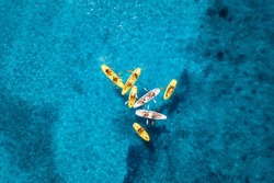 Aerial View Of Yellow Kayaks In Blue Sea At Sunset In Summer. People On Floating Canoes In Clear Azure Water. Sardinia Island, Italy. Tropical Landscape. Sup Boards. Active Travel. Top View From Drone