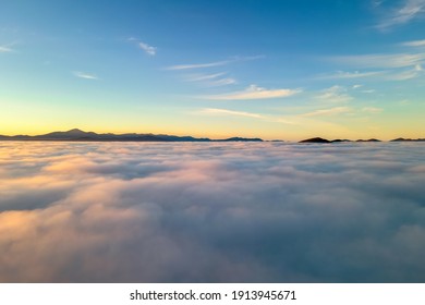 Aerial view of yellow sunset over white puffy clouds with distant mountains on horizon.