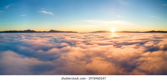 Aerial view of yellow sunset over white puffy clouds with distant mountains on horizon. - Shutterstock ID 1976960147