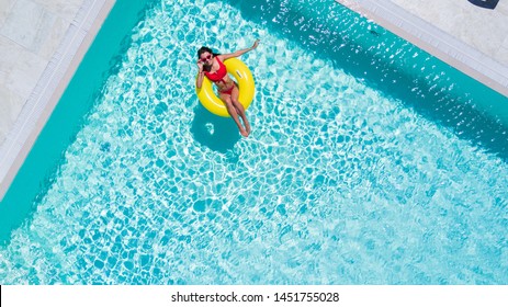 Aerial View Of Young Brunette Woman Swimming On The Inflatable Big Yellow Ring In Pool