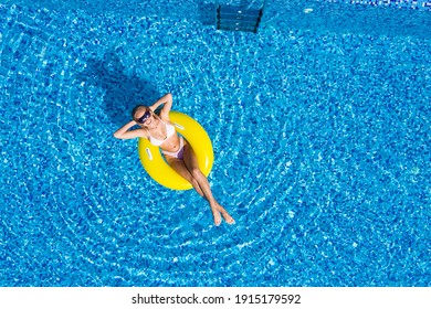 Aerial view of young brunette woman swimming on the inflatable big yellow ring in pool
