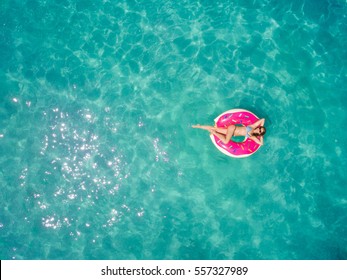 Aerial view of young brunette woman swimming on the inflatable big donut in the transparent turquoise sea. Top view of slim lady relaxing on her holidays in Thailand, Phuket, Andaman sea.