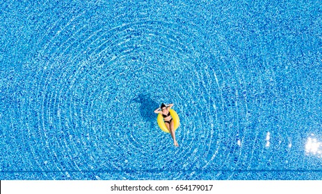 Aerial View Of Young Brunette Woman Swimming On The Inflatable Big Yellow Ring In Pool