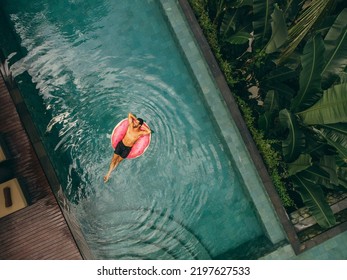 Aerial view of young man relaxing on inflatable ring in resort swimming pool. Male enjoying holidays at luxury resort. - Powered by Shutterstock