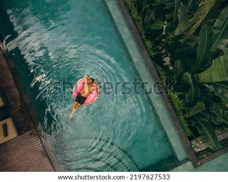 Aerial view of young man relaxing on inflatable ring in resort swimming pool. Male enjoying holidays at luxury resort.