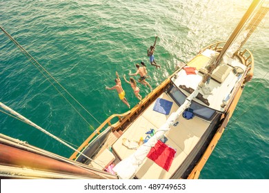 Aerial View Of Young People Jumping From Sailing Boat On Sea Trip - Rich Happy Friends Having Fun In Summer Party Day - Exclusive Vacation Concept - Warm Vintage Filter With Enhanced Sun Flare Halos