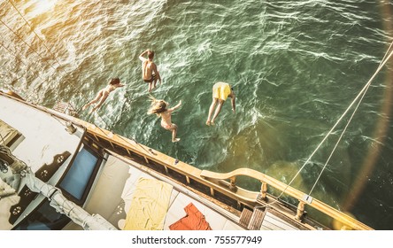 Aerial View Of Young People Jumping From Sailing Boat On Sea Trip - Rich Happy Friends Having Fun In Summer Sailboat Party Day - Exclusive Luxury People Vacation Concept - Warm Retro Sunshine Filter