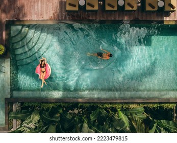 Aerial view of young woman relaxing on inflatable ring and man swimming in resort pool. Couple enjoying holidays at luxury resort. - Powered by Shutterstock