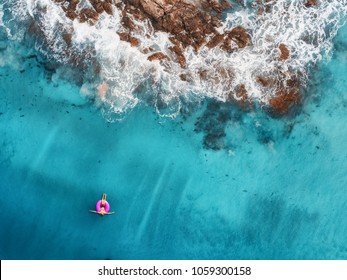 Aerial view of young woman swimming on the pink swim ring in the transparent turquoise sea in Maldives.  Top view. Nature