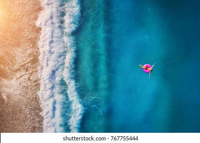 Aerial view young woman swimming the pink swim ring in the transparent turquoise sea in Oludeniz  Summer seascape and girl  beach  beautiful waves  blue water at sunset  Top view from drone