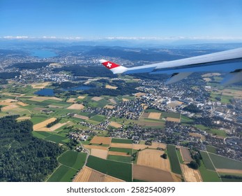 Aerial view of Zurich, Switzerland, from an airplane window, showcasing the Swiss countryside, city skyline, and Zurich Lake with a aircraft wing in the foreground.