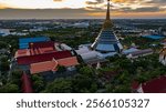 An aerial Wat Ketmadi Sriwararam perspective showcasing a stunning Thai temple complex with intricate golden spires, surrounded by urban and rural landscapes under a cloudy blue sky.