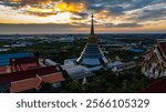 An aerial Wat Ketmadi Sriwararam perspective showcasing a stunning Thai temple complex with intricate golden spires, surrounded by urban and rural landscapes under a cloudy blue sky.