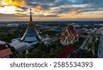 An aerial Wat Ketmadi Sriwararam perspective showcasing a stunning Thai temple complex with intricate golden spires, surrounded by urban and rural landscapes under a cloudy blue sky.