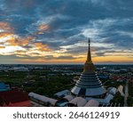 An aerial Wat Ketmadi Sriwararam perspective showcasing a stunning Thai temple complex with intricate golden spires, surrounded by urban and rural landscapes under a cloudy blue sky.