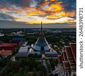 An aerial Wat Ketmadi Sriwararam perspective showcasing a stunning Thai temple complex with intricate golden spires, surrounded by urban and rural landscapes under a cloudy blue sky.