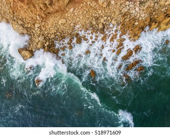 Aerial. Waves swim to the rocky shore.