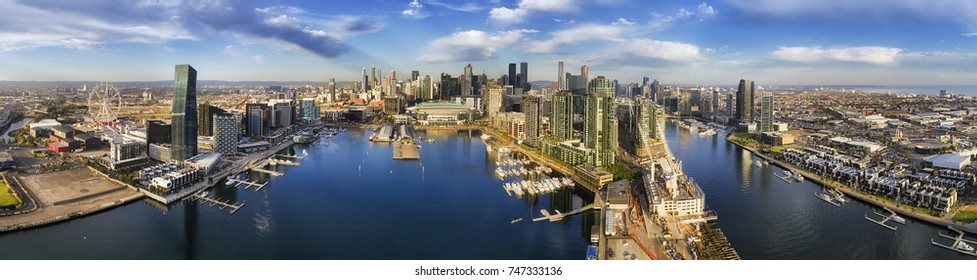 Aerial wide panorama of Melbourne Docklands area over Yarra river waters with marina yachts and wharfs. Modern urban high-rise towers and architecture on CBD waterfront.