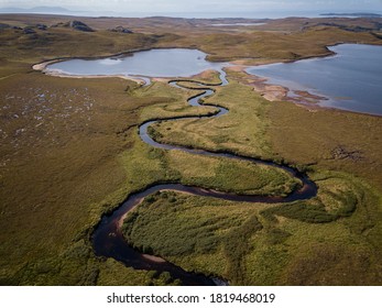 Aerial of a wild creek winding its way through a lush green Glen in the Scottish highlands