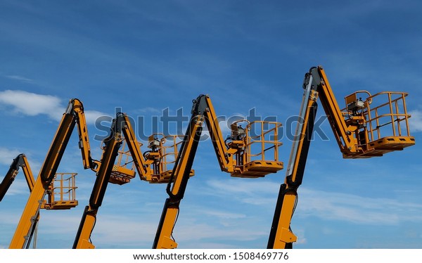 Aerial work platforms lined up against blue sky\
with clouds
