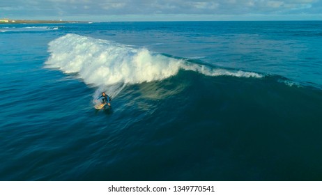 AERIAL: Young Male Surfer Carving A Tube Wave Glistening In Bright Sunshine. Sportsman On Awesome Surfboard Rides A Metallic Blue Ocean Wave. Barrel Wave Reflecting Summer Sunshine Like A Mirror.