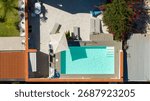 Aerial zenithal view of an empty rectangular pool. The pool is located in the garden of a beautiful house. There are steps to enter the water and loungers surrounding the pool.
