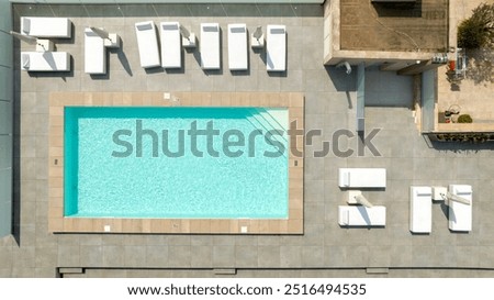Aerial zenithal view of an empty swimming pool. There are white sun loungers. No one is in the garden.