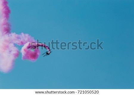 Aerobatic plane leaving a pink smoke trail in the bright blue sky.
