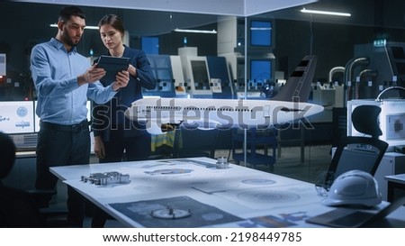 Aeronautics Factory Office Meeting Room: Engineer Holds Tablet Computer, Showing Augmented Reality Airplane Jet Engine to a Female Project Manager. Modern Industry 4.0 Research and Development Test.