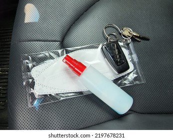 An Aerosol Bottle Containing Hand Sanitizer, White Medical Mask, Car Remote And Key Chain, Placed On Black Car Seat. Necessary Device When Leaving  House During Epidemic Of Covid-19 And Monkeypox .