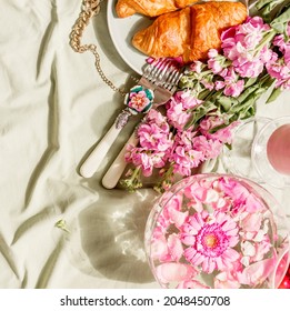 Aesthetic Breakfast With Croissant And Pink Flowers Bunch On Light Green Blanket At Sunshine. Top View