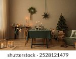 Aesthetic composition of warm dining room interior with table, green tablecloth, christmas tree, wreath, candle, wooden console, glass, gifts and personal accessories. Home decor. Template.