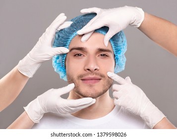 Aesthetic Cosmetology Concept. Doctor's Hands In Gloves Touching Face Of Handsome Young Man, Closeup