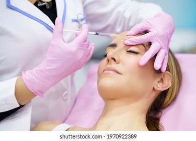 Aesthetic Doctor Injecting Botulinum Toxin Into The Forehead Of Her Middle-aged Patient.