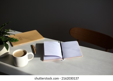 Aesthetic home office desk table. Feminine workspace with paper notebook, cup of coffee, plant, chair in sunlights