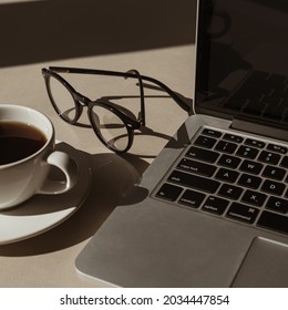 Aesthetic Luxury Bohemian Minimalist Home Office Workspace Desk. Laptop Computer, Cup Of Coffee, Glasses With Sunlight Shadows. Flat Lay, Top View Work, Business Concept