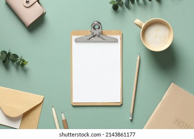 Aesthetic minimal office desk table with clipboard mockup, coffee cup, stationery and eucalyptus leaves on green background. Flat lay, top view.