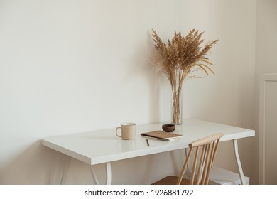 Aesthetic Minimal Office Workspace Interior Design. Mug, Notebook, Pampas Grass Floral Bouquet On White Table Against White Wall. Girl, Woman Boss Work At Home Business Concept.