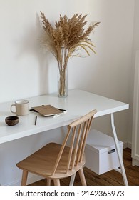 Aesthetic Minimal Office Workspace Interior Design. Chair And Table. Mug, Notebook, Pampas Grass Floral Bouquet On White Table Against White Wall. Girl, Woman Boss Work At Home Business Concept