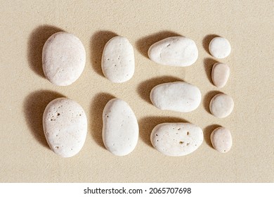Aesthetic minimal pattern with set of pebble stones on fine sand background. Square composition from natural stone neutral beige color.  Summer concept of harmony, balance, relax. Top view, flat lay.