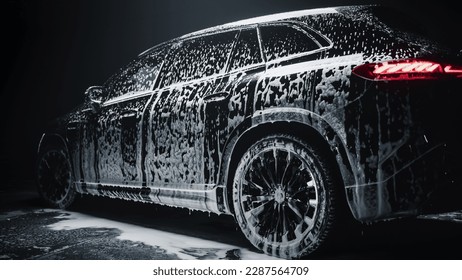 Aesthetic Photo of a Black Family SUV Covered in Washing Soap and Foam. Close Up Shot of Foam Dripping from Car's Rear Wheel Arch onto the Electric Car's Tyre and Rim