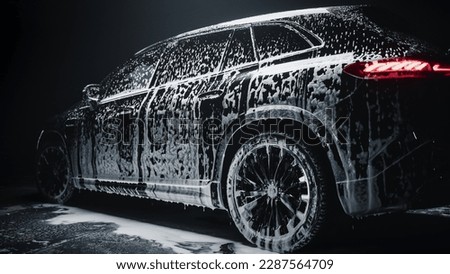 Aesthetic Photo of a Black Family SUV Covered in Washing Soap and Foam. Close Up Shot of Foam Dripping from Car's Rear Wheel Arch onto the Electric Car's Tyre and Rim