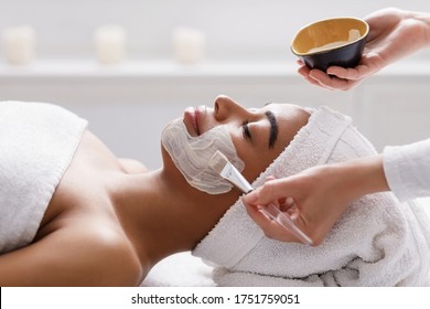 Aesthetic Procedure. Beautician Applying Clay Face Mask On Black Woman Face, Side View